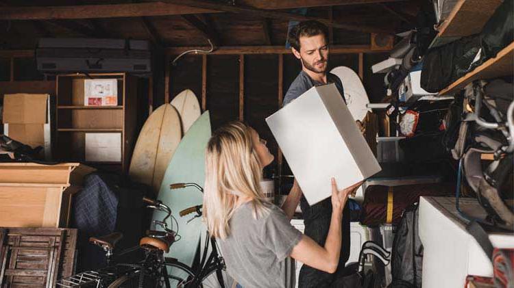 Woman h和ing man a box in garage for storage.